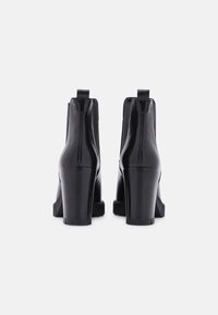 Bottines en cuir noir avec un bout rond, un talon bloc haut, des panneaux élastiques sur les côtés et des languettes à l'arrière pour un enfilage facile. Texture lisse et design minimal.
