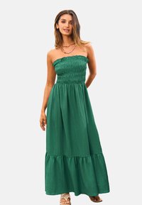 Abito lungo verde senza spalline con corpetto arricciato, gonna fluida e orlo a strati. Realizzato in tessuto leggero con una finitura testurizzata.