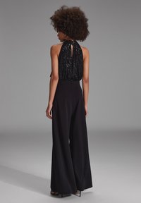 Czarny halter top z cekinami i wycięciem na plecach, w zestawie z szerokimi czarnymi spodniami. Gładka tekstura i zwiewny fason.