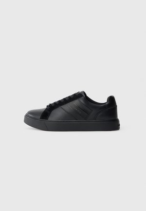 Black leather sneaker with a smooth finish, textured side panels, round toe, flat sole, and logo detail on the side. Features classic lacing.