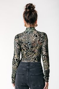 Haut en mesh à manches longues de couleur verte avec un motif animal, col montant et silhouette ajustée, associé à un jean noir taille haute.