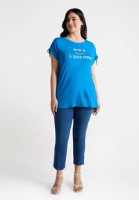 Camiseta azul de manga corta con mangas atadas y una frase impresa en blanco, combinada con pantalones azul de tiro ankle y sandalias ligeras con tiras.