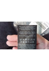 Černá textilní etiketa s pokyny k praní a složením materiálu: 92 % polyester, 8 % nylon, se symboly péče v několika jazycích.