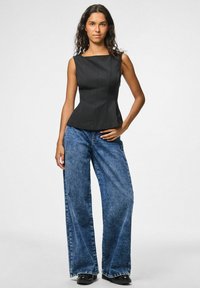 Débardeur noir ajusté avec un décolleté carré et des coutures verticales, associé à un jean en denim bleu à jambes larges et des chaussures noires.