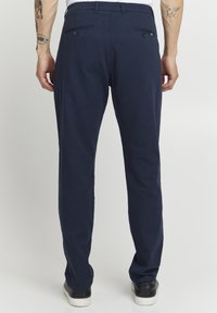 Herre navy bukser med en glat tekstur, slim fit, to baklommer med knapper og ankel-længde kant, parret med sorte sko.