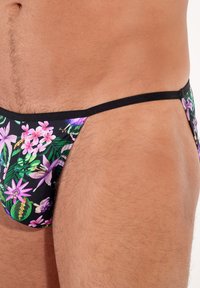 Schwarze Badebadehose mit floralem Druck in Lila- und Grüntönen. Minimalistisches Design mit dünnen Seitenstreifen und einer glatten Textur.