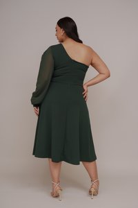 Robe verte avec un design asymétrique sur une épaule. Une manche est longue et transparente, le tissu est lisse. La robe s'évasent au niveau des genoux, avec une fermeture éclair.