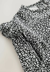 Schwarz-weißes Leopardenmuster-Kleid aus weichem Stoff mit rüschierten Ärmeldetails und rundem Ausschnitt. Das Muster besteht aus variierenden Flecken.