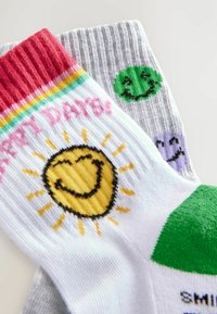 Calzini di cotone colorati, con un calzino bianco decorato con una grafica del sole e un calzino grigio con faccine sorridenti verdi e viola. Texture a coste e accenti multicolori.