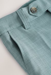 Hellblauer, strukturierter Stoff einer Hose mit einer vorderen Klappe und einem Knopf sowie sichtbaren Nähten entlang der Kanten.