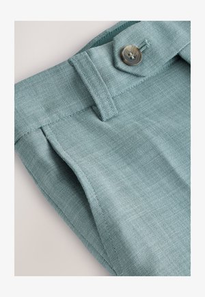 Jasnoniebieska teksturowana tkanina spodni, z przednią klapką zapinaną na guzik oraz widocznym przeszyciem wzdłuż krawędzi.