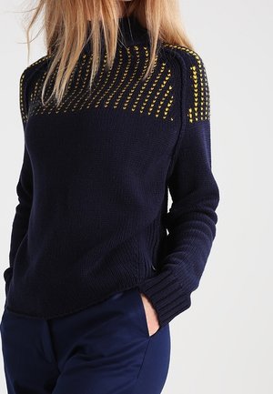Maglione lavorato a maglia blu navy con collo alto, corpo testurizzato e un motivo decorativo giallo sulle spalle. Design fitted con polsini a coste.