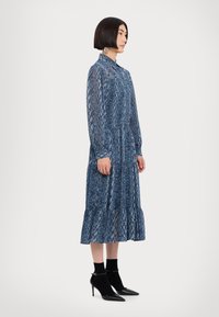 Rochie bleu cu imprimeu de șarpe, confecționată din material transparent, având mâneci lungi, guler înalt și un tiv evazat, asociată cu cizme negre până la gleznă.