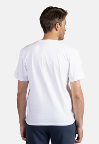 Bílý bavlněný tričko s krátkým rukávem, kulatým výstřihem a hladkou texturou, pohled z zadní strany, ukazující jednoduchý design.