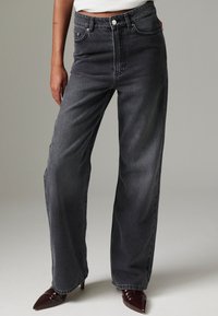 Traperice visokog struka širokih nogavica u tamnosivoj boji s izblijedjelim efektom, s prednjim džepovima i metalnim dugmadima kao ukrasom.