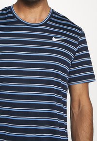 Muž oblečený v modro-navy a světle modrém pruhovaném tričku s krátkým rukávem a kulatým výstřihem značky Nike.