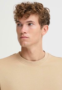 Beige cotton crewneck t-shirt with a textured finish, displaying a close-up of the neckline and upper body, featuring short sleeves.