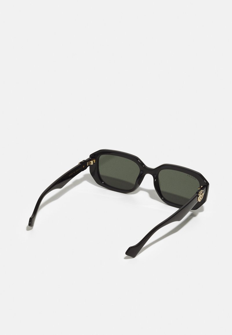 Schwarze Sonnenbrille mit quadratischen Gläsern, grünem Tint und glänzender Oberfläche. Verfügt über goldene Beschläge am Rahmen und schlanke Bügel.
