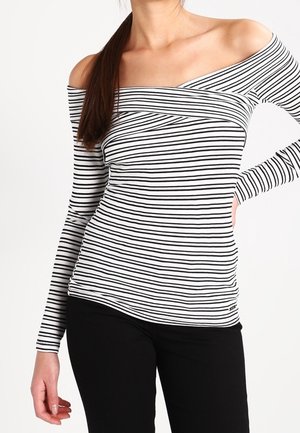 Haut à rayures noires et blanches à épaules dénudées, à manches longues, avec une coupe cintrée et une texture douce ; associé à un pantalon noir.
