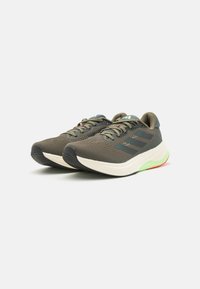 Des chaussures de course avec une tige en maille de couleur olive, rehaussées d'accents noirs et vert clair. Semelle épaisse avec des éléments rouges et verts sur la semelle extérieure.