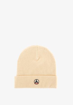 Beige knit beanie with folded cuff and small circular black, white, and red logo patch featuring a seated figure and "JOTT" text on the front.