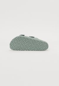 Chaussure slip-on vert menthe avec bout arrondi et semelle en caoutchouc texturée présentant des motifs en tourbillon. Deux sangles ajustables sur le dessus.