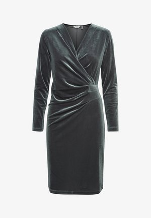 Donkergroene fluwelen jurk met lange mouwen, v-hals en geraffineerde details bij de taille. Gladde textuur en getailleerd silhouet.