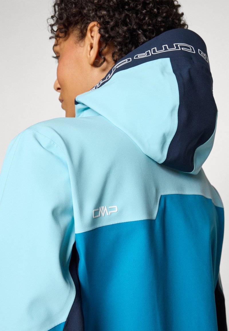 Eine zweifarbige blaue Jacke mit Kapuze, die eine glatte Textur aufweist. Der Kragen ist marineblau, und ein weißes "CMP"-Logo ist an der Seite sichtbar.
