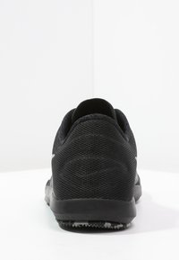 Black athletic shoe featuring a textured mesh upper, rounded heel, and rubber outsole with a patterned grip. Rear view showcases seamless design.