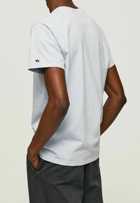 Jasnoniebieska bawełniana koszulka z krótkim rękawem, okrągłym dekoltem i haftowanym logo na lewym rękawie, zestawiona z ciemnoszarymi szortami.