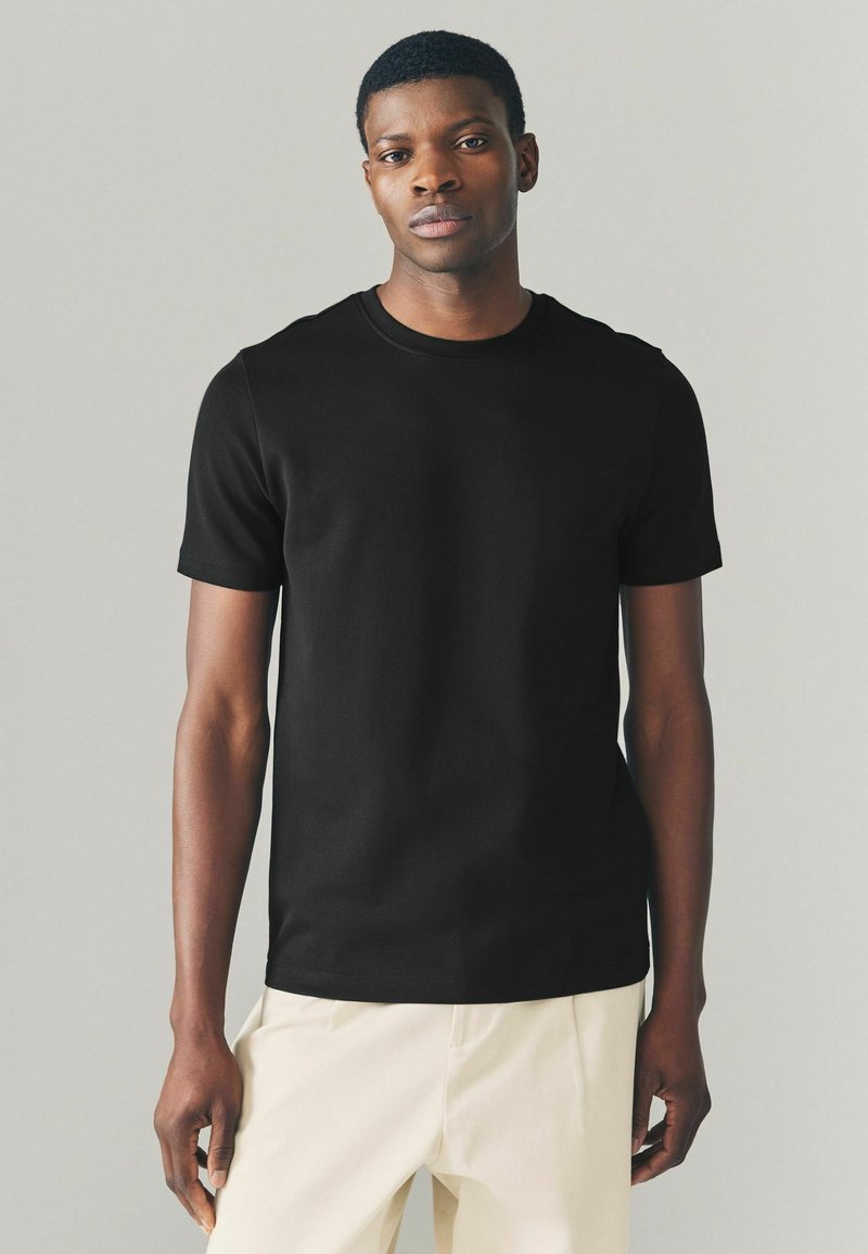 Sort bomulds T-shirt med korte ærmer, rund halsudskæring og en tætsiddende silhuet, parret med lyse bukser. Glat tekstur.