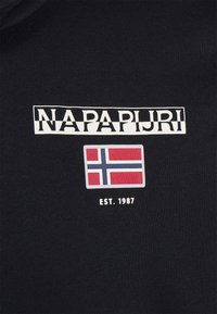 Un tejido negro presenta el logotipo "NAPAPIJRI" en blanco, un gráfico de la bandera noruega en rojo, blanco y azul, y "EST. 1987" debajo.