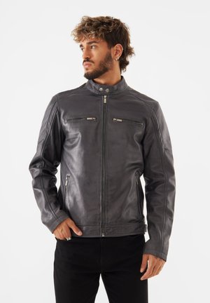 Chaqueta de cuero gris para hombre, diseño estructurado, cuello alzado, dos bolsillos con cremallera en el pecho, textura suave y silueta ajustada.