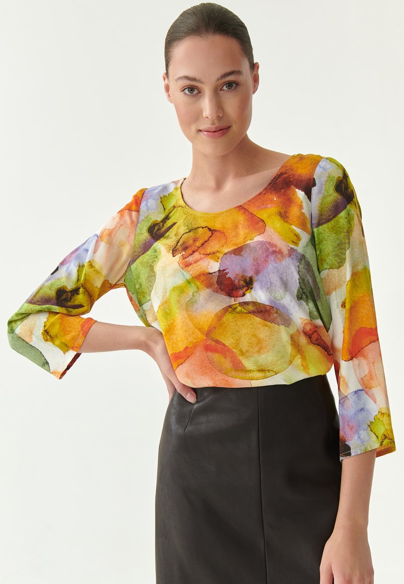 Multikleurige, lichte blouse met een ronde halslijn en driekwartmouwen, met een aquarelpatroon in groen, oranje en paars.