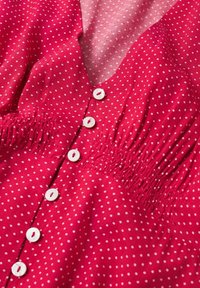 Tissu rouge à petits pois blancs, boutons blancs au centre et détails élastiques froncés à la taille.