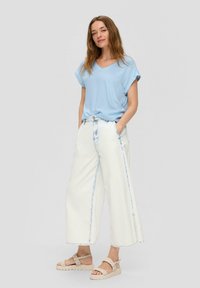 Lichtblauw, T-shirt met korte mouwen en V-hals, gecombineerd met brede, witte denim broek met lichtblauwe stiksels en lichtbeige sandalen.