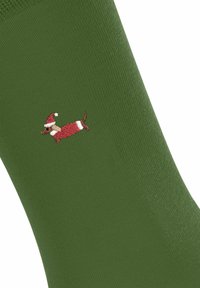 Grüne Socke mit einem gestickten Dackel, der einen Weihnachtsmann-Hut trägt, der spielerisch an der Seite der Socke positioniert ist.