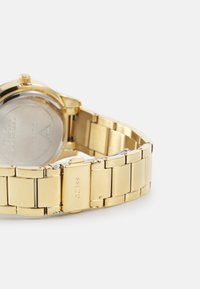 Gouden metalen horloge met een ronde kast, gepolijste en geborstelde afwerkingen op de band, en een stevige sluiting met het merklogo.