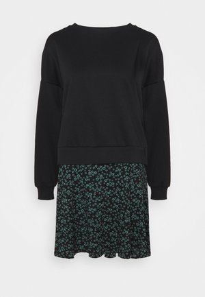 Pull noir à manches longues associé à une jupe noire avec un petit motif floral vert.
