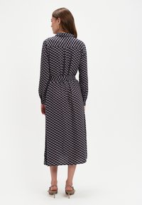 Granatowa sukienka koszulowa w wzór, z długimi rękawami, wcięciem w talii i długości do połowy łydki, z geometrycznym wzorem i detalami w postaci guzików.