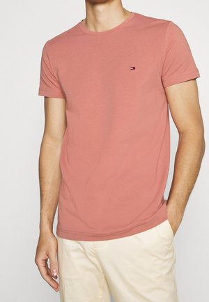 Helles rosa Baumwoll-T-Shirt mit rundem Halsausschnitt und kurzen Ärmeln, das ein kleines Logo auf der Brust und einen geraden Saum aufweist.