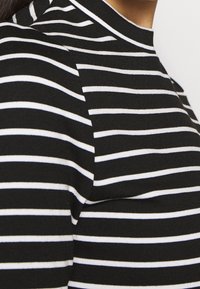 Czarna i biała bluzka w paski z wysokim kołnierzem. Materiał wydaje się miękki i rozciągliwy, z poziomymi paskami o równej szerokości.