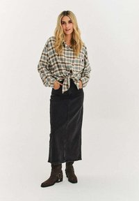 Károvaná košeľa v béžovej a zelenej farbe, zviazaná v páse; čierna džínová maxi sukňa; hnedé členkové čižmy so zapínaním na pracku.