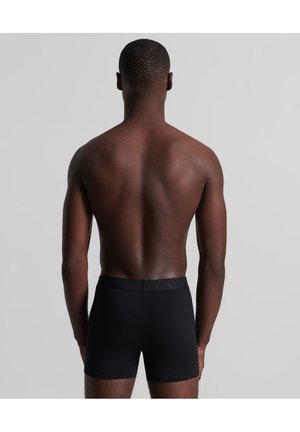 Boxers noirs avec un design ajusté et une taille élastique, portant le nom de la marque "SUPERDRY" en texte noir contrasté.