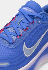 Μπλε αθλητικό παπούτσι με υφασμάτινο άνω μέρος με υφή, γκρίζες και ροζ λεπτομέρειες, έντονο λογότυπο και αντίθετες σόλες. Διαθέτει μαξιλαρωτή σόλα.