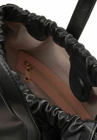 Borsa tote nera in pelle con una parte superiore arricciata, foderata in un beige chiaro e dotata di una piccola tasca con zip, accentuata da una cerniera dorata.