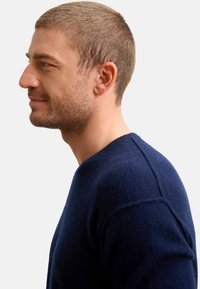 Maglione di lana blu navy con scollatura rotonda, colletto a coste e una consistenza sottile. Il modello è mostrato in vista profilo.