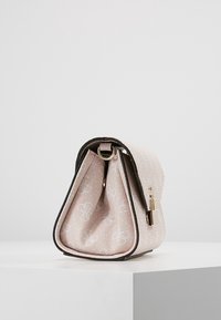 Jasnoróżowa torebka w wzory z złotym zapięciem i ciemnym wykończeniem, stojąca pionowo na białej powierzchni na tle jednolitego tła.