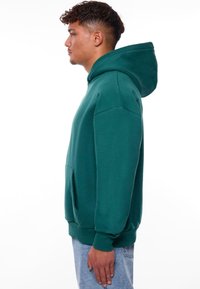 Sweat à capuche teal avec une poche kangourou, des poignets côtelés et une coupe décontractée. Tissu doux avec une texture lisse.