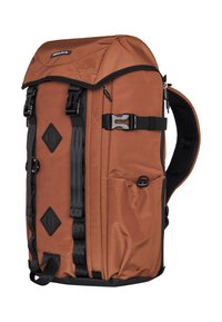 Mochila de tela marrón con una solapa superior, múltiples correas de ajuste, bolsillos laterales y acentos de hardware negro. Presenta detalles de material texturizado.